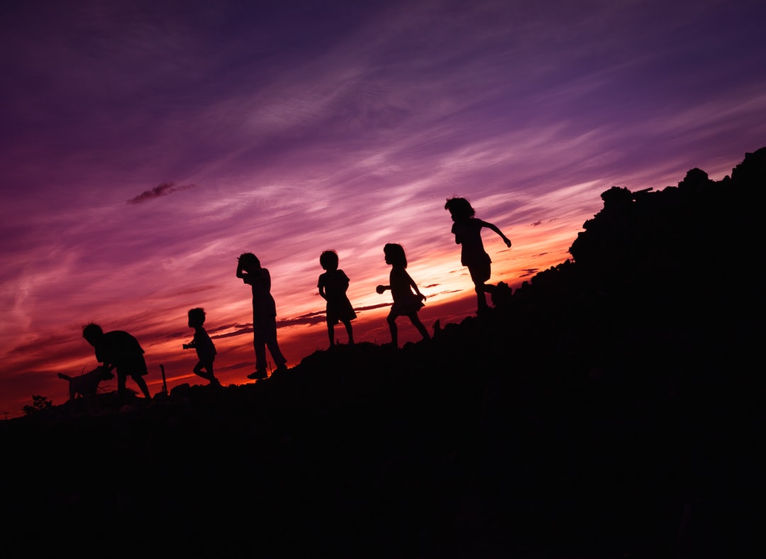 A group of people walking up a hill with a sunset in the background